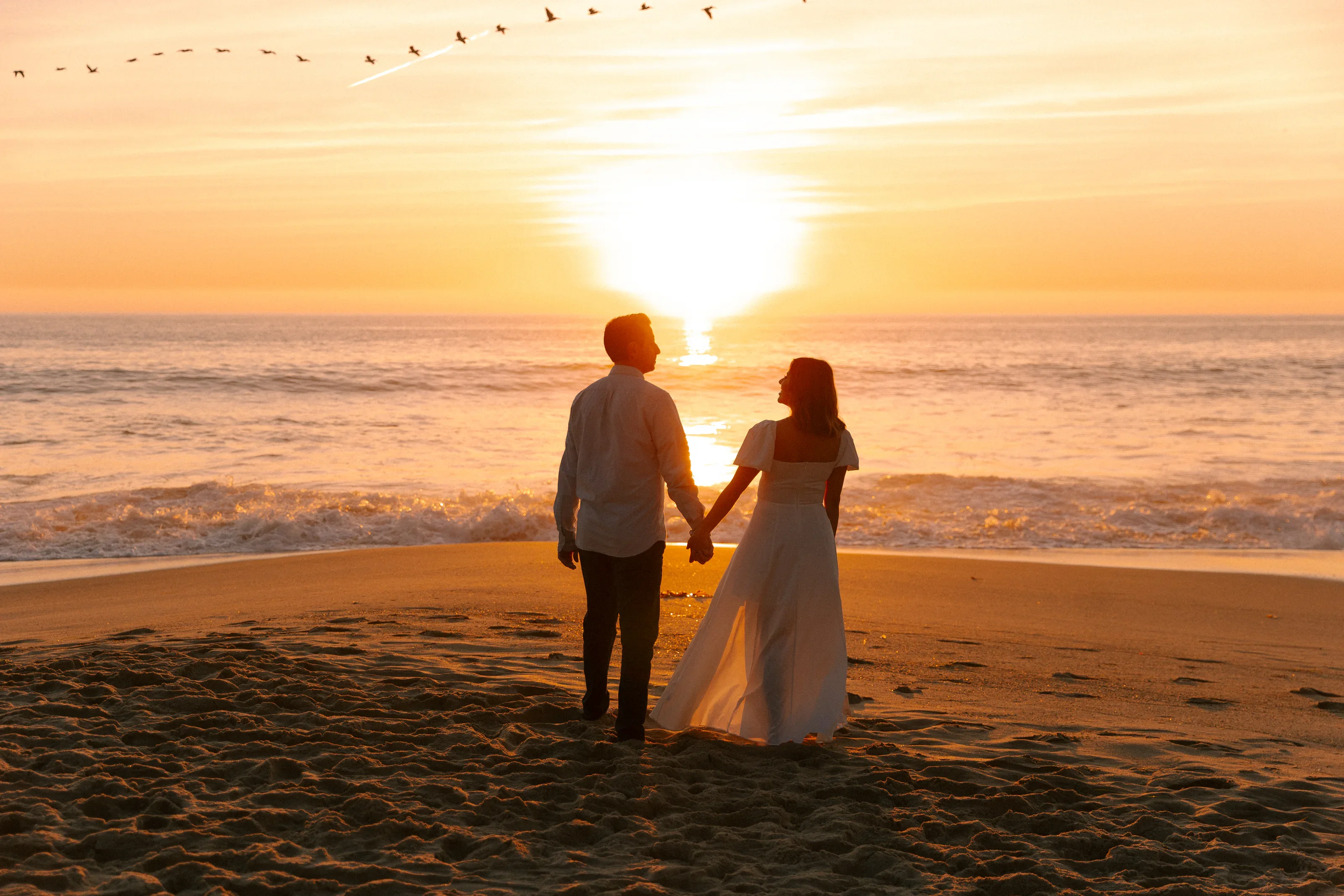 Wide cinematic engagement portrait against the ocean sunset