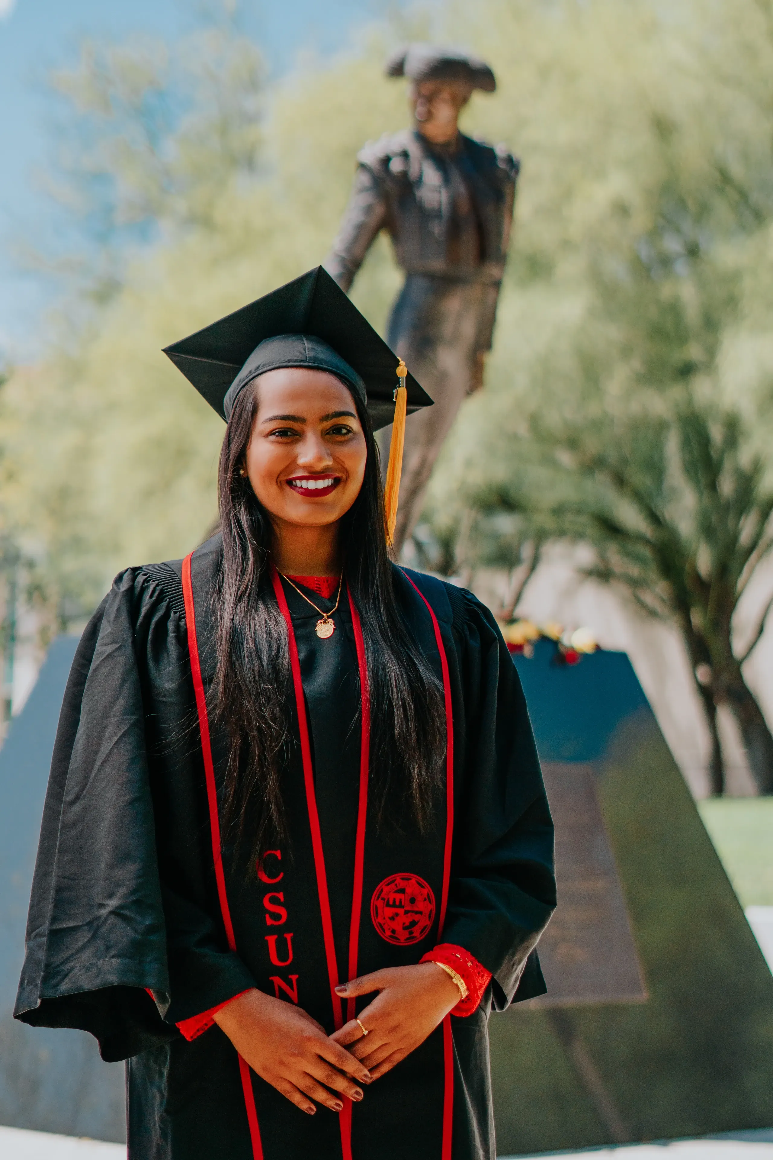 Cal State Fullerton graduate in gown, honors cords, and red stole