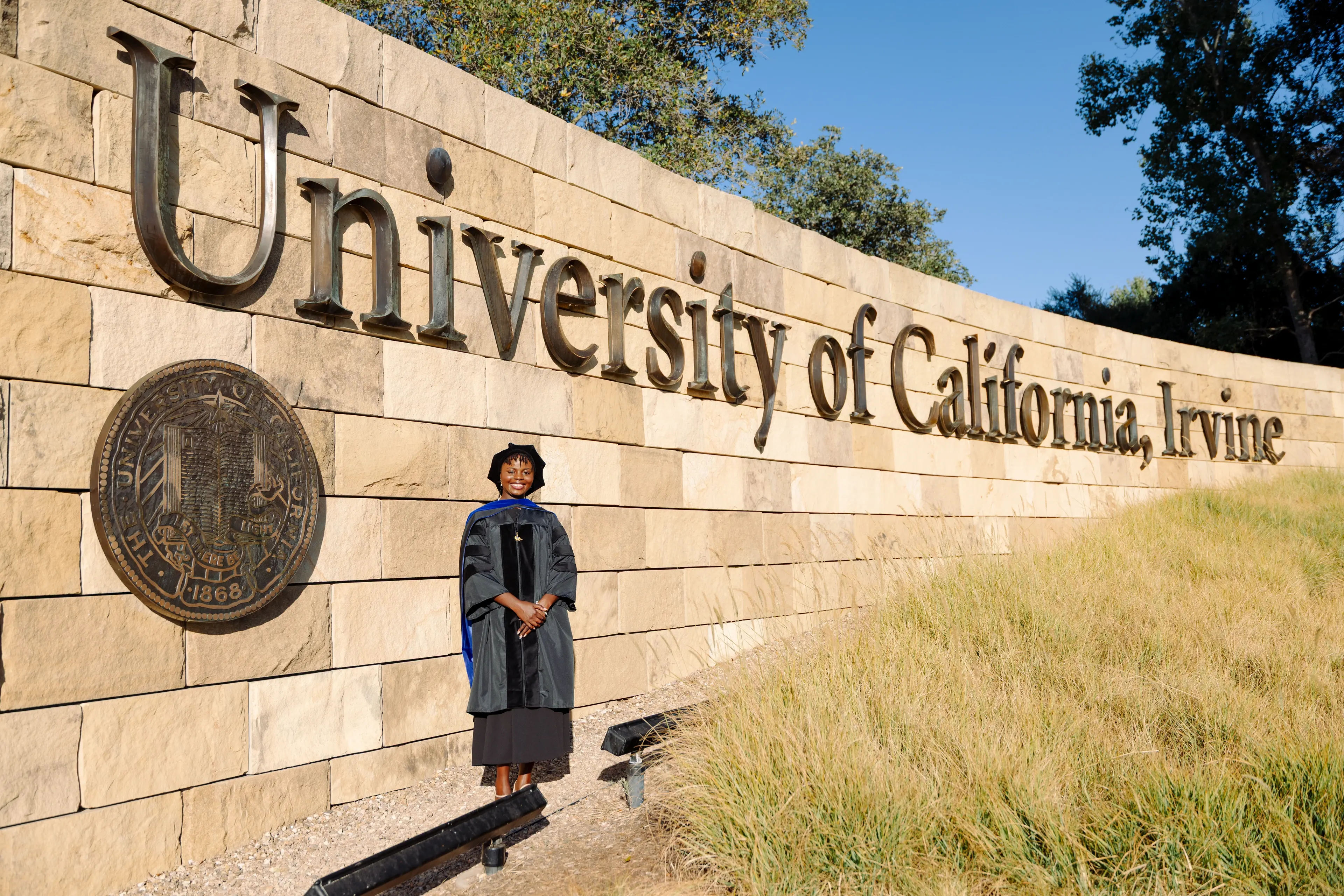 UC Irvine graduate photographed beside the University of California Irvine campus sign