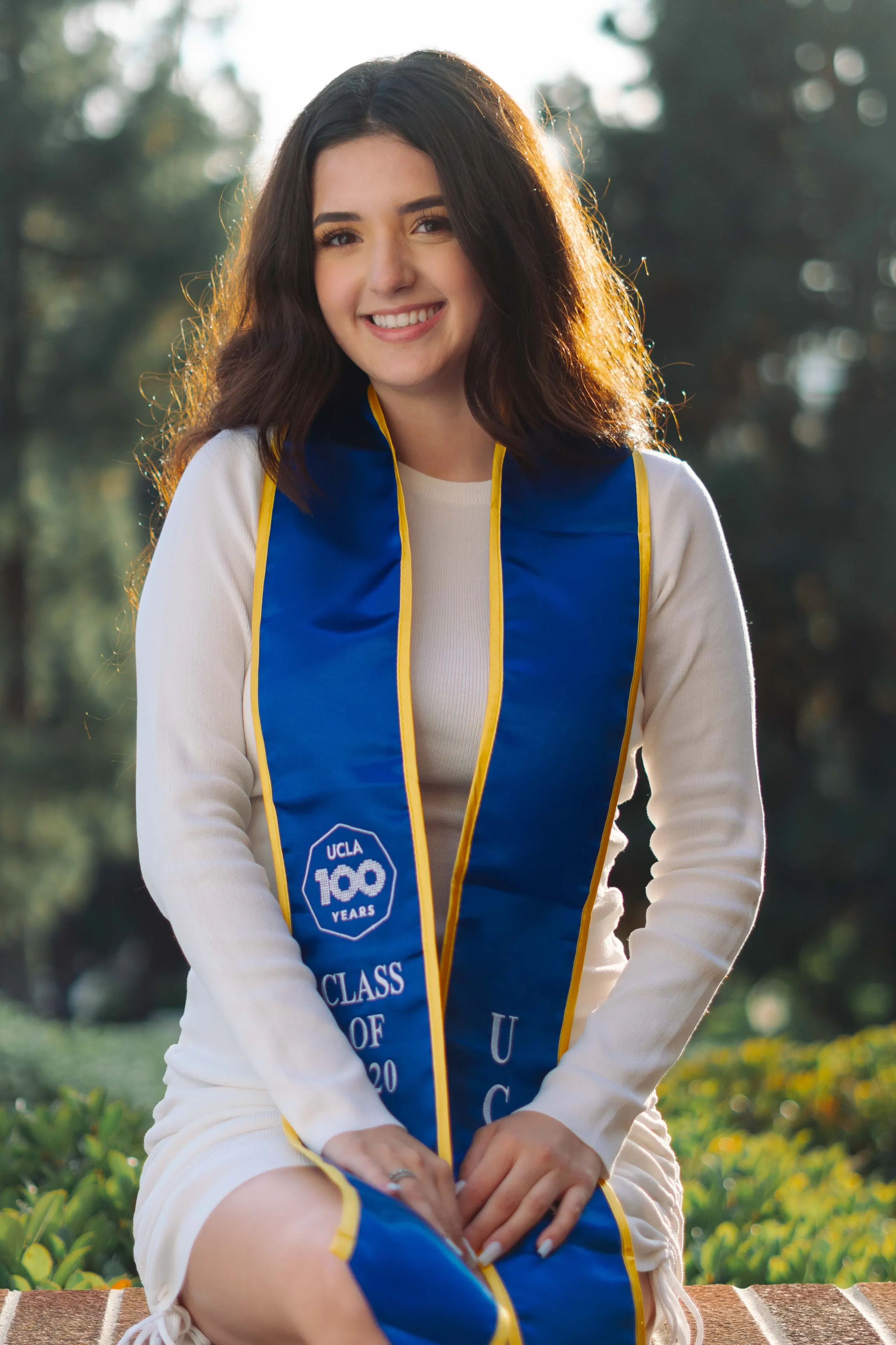UCLA graduate smiling in a blue and gold commencement stole at golden hour