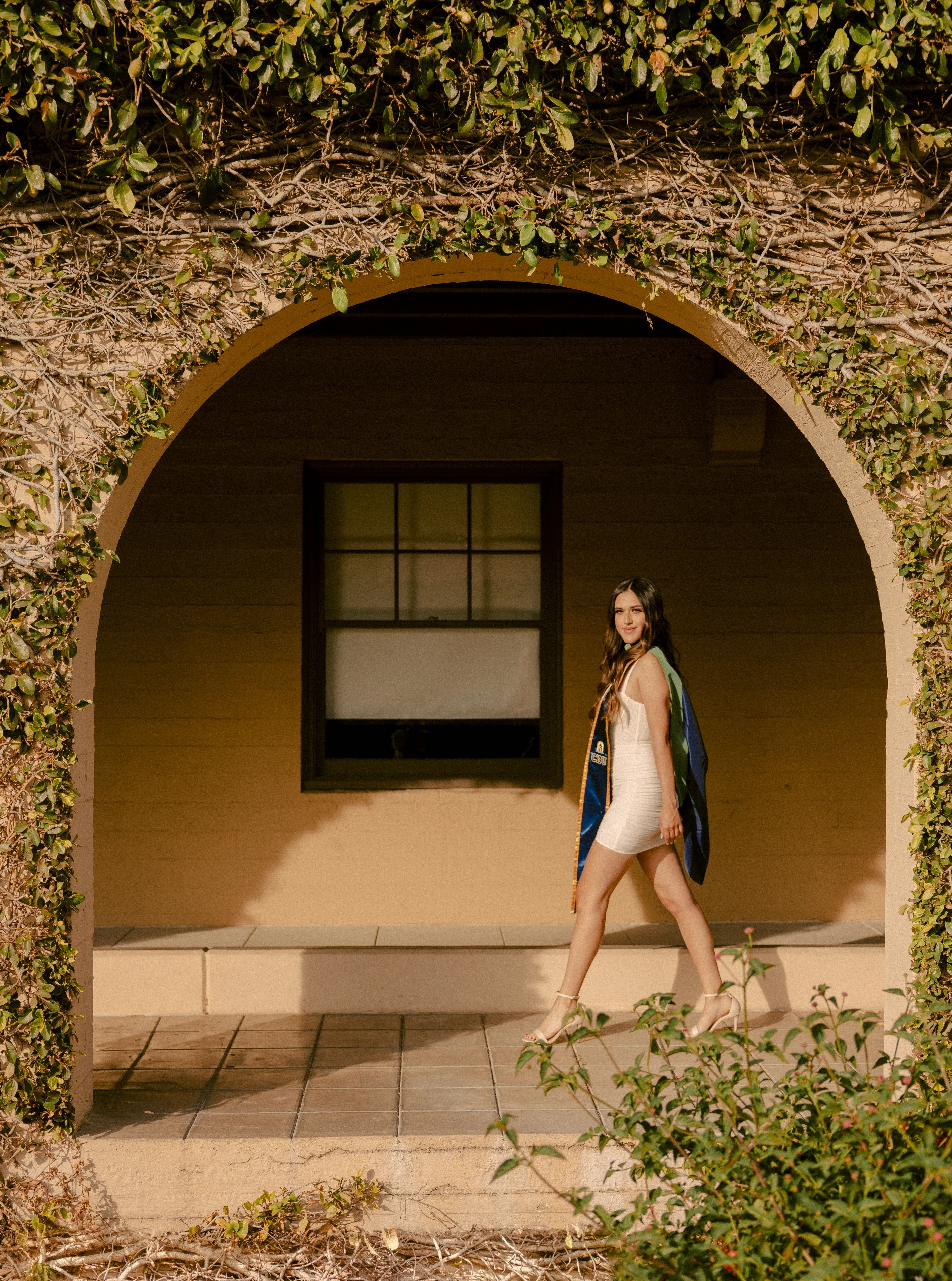 UCLA graduate walking beside an ivy-covered campus building