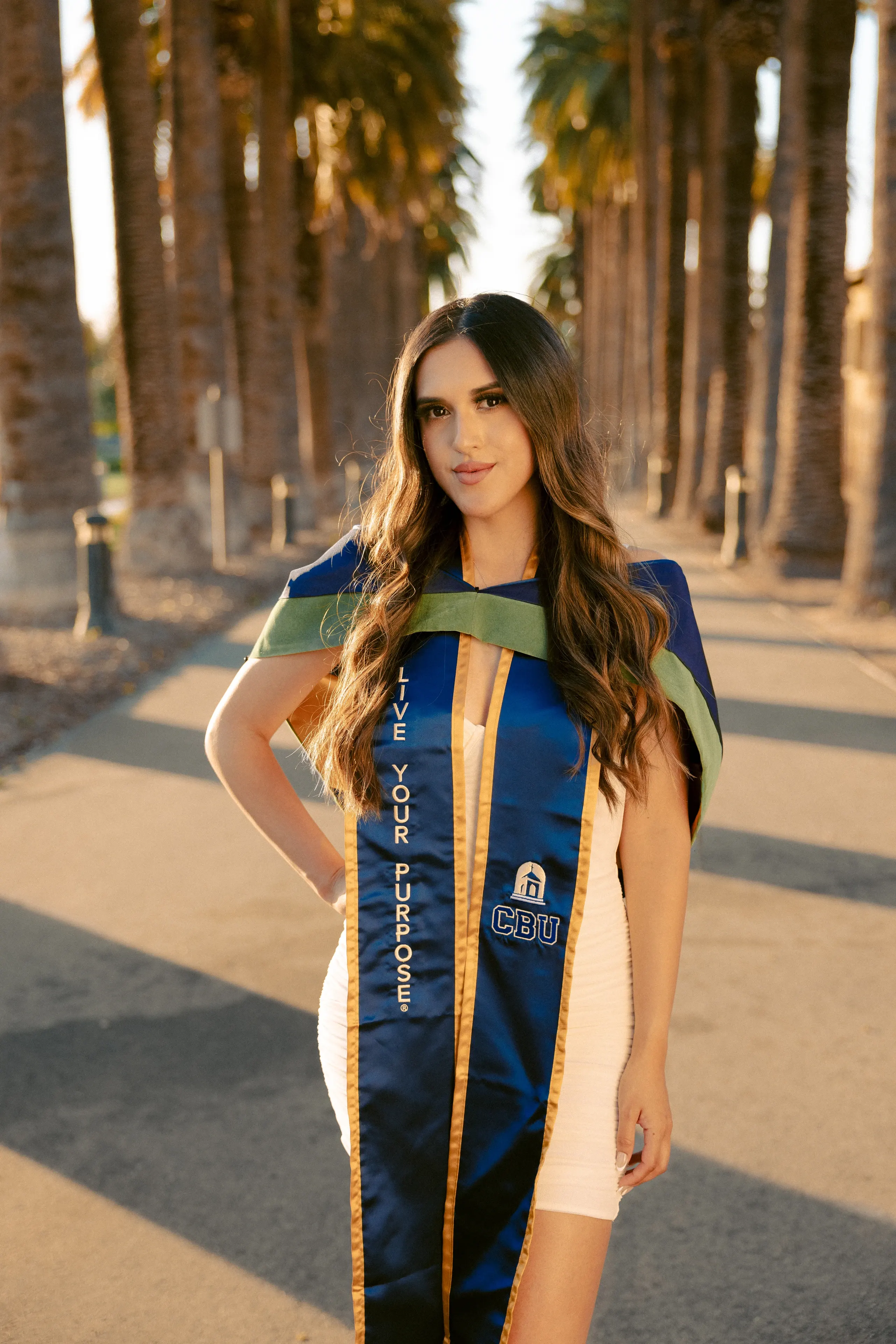 UCLA graduate photographed along a palm-lined campus walkway