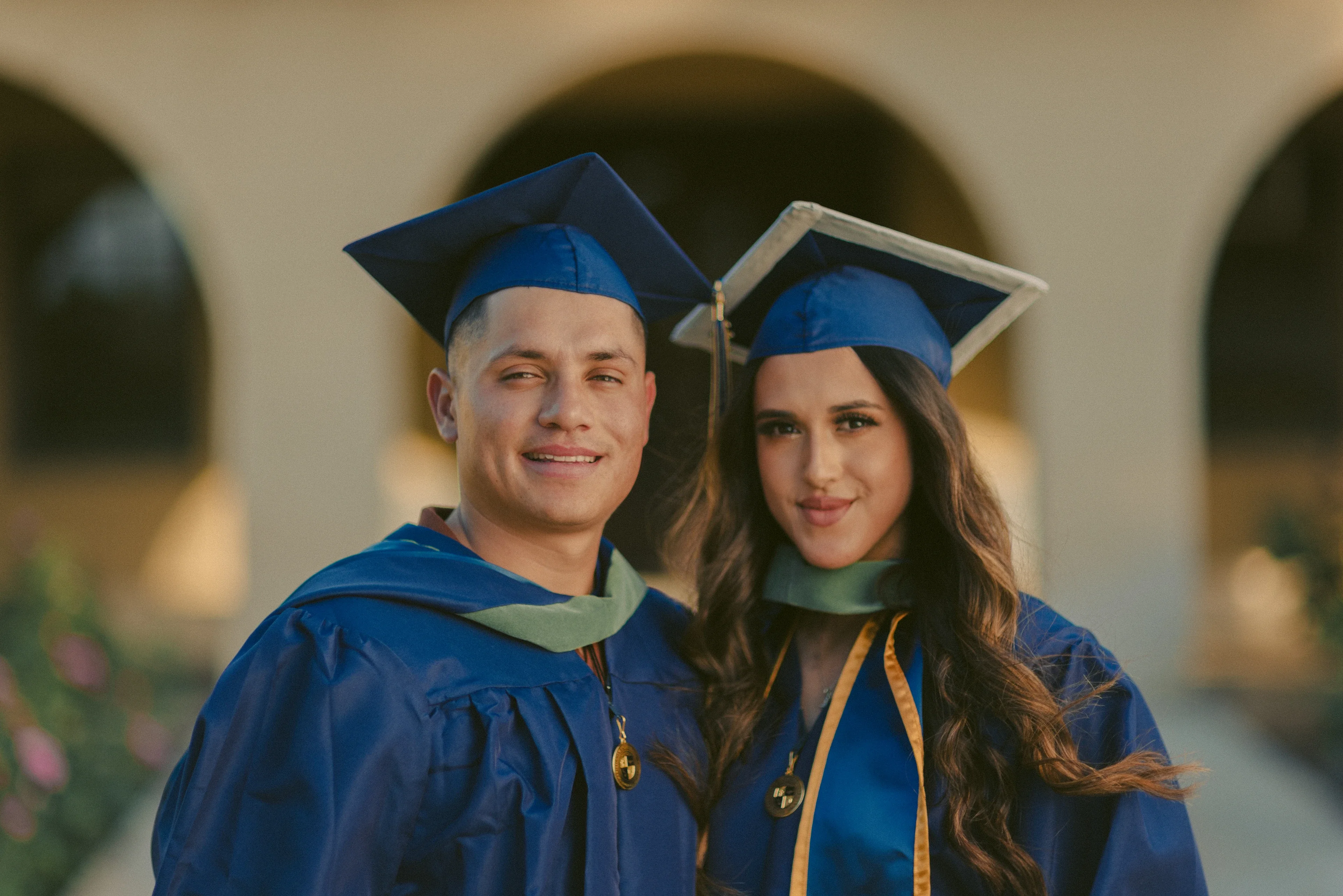 Two UCLA graduates posing together in caps, gowns, and stoles