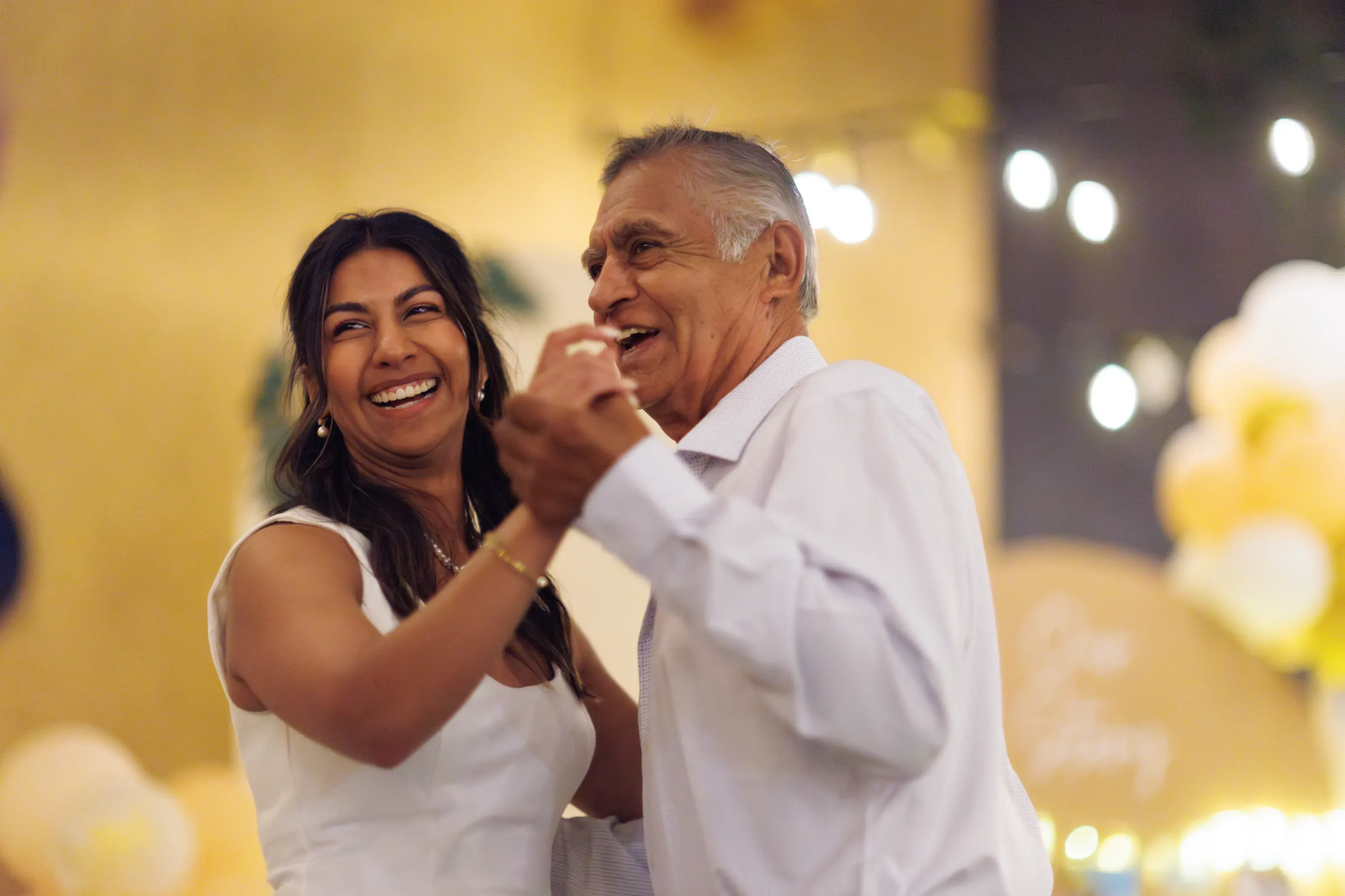 Joyful parent dance beneath warm reception lights